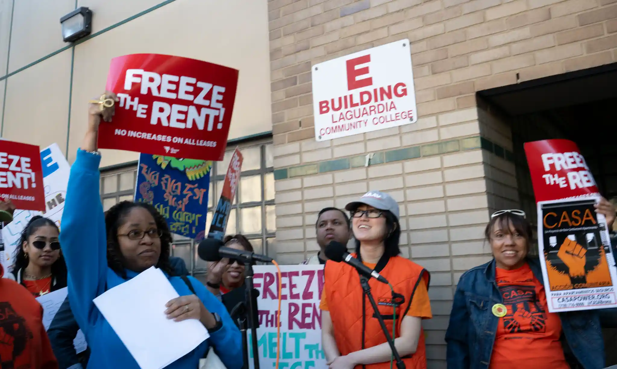 Protesters outside LaGuardia Community College with red 'Freeze the Rent' signs, near the E Building sign.