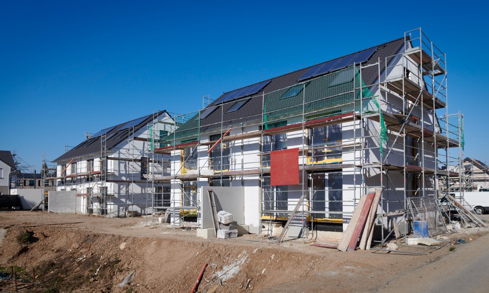Row of new houses under construction with metal scaffolding and a clear blue sky.