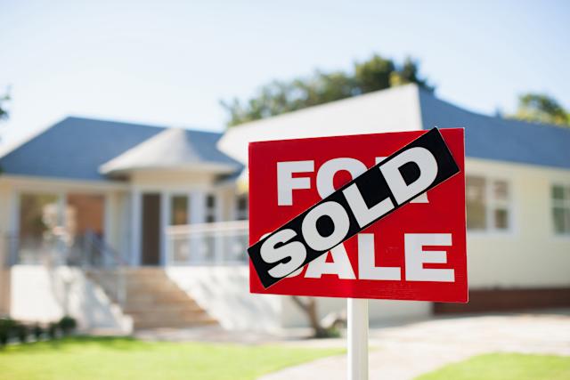 Red 'FOR SALE' real estate sign with a diagonal black 'SOLD' banner in front of a suburban house yard.