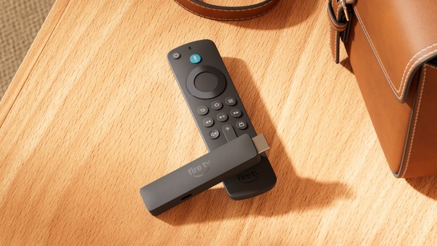 Fire TV remote with dongle attached, resting on a wooden table beside a brown leather bag.