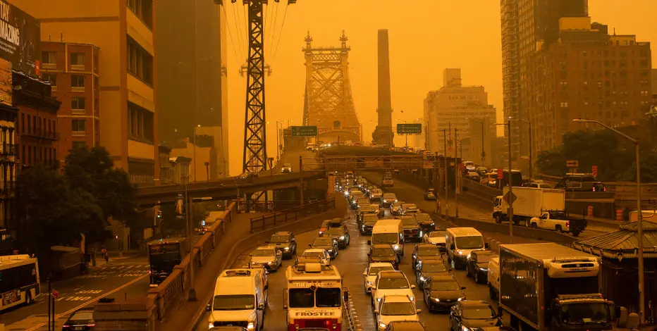 Heavy traffic on a multi-lane city street with a distant bridge under orange sunset lighting.