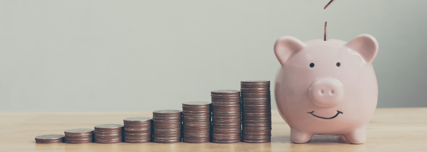 Pink piggy bank sits beside ascending stacks of coins on a wooden surface, illustrating savings growth.