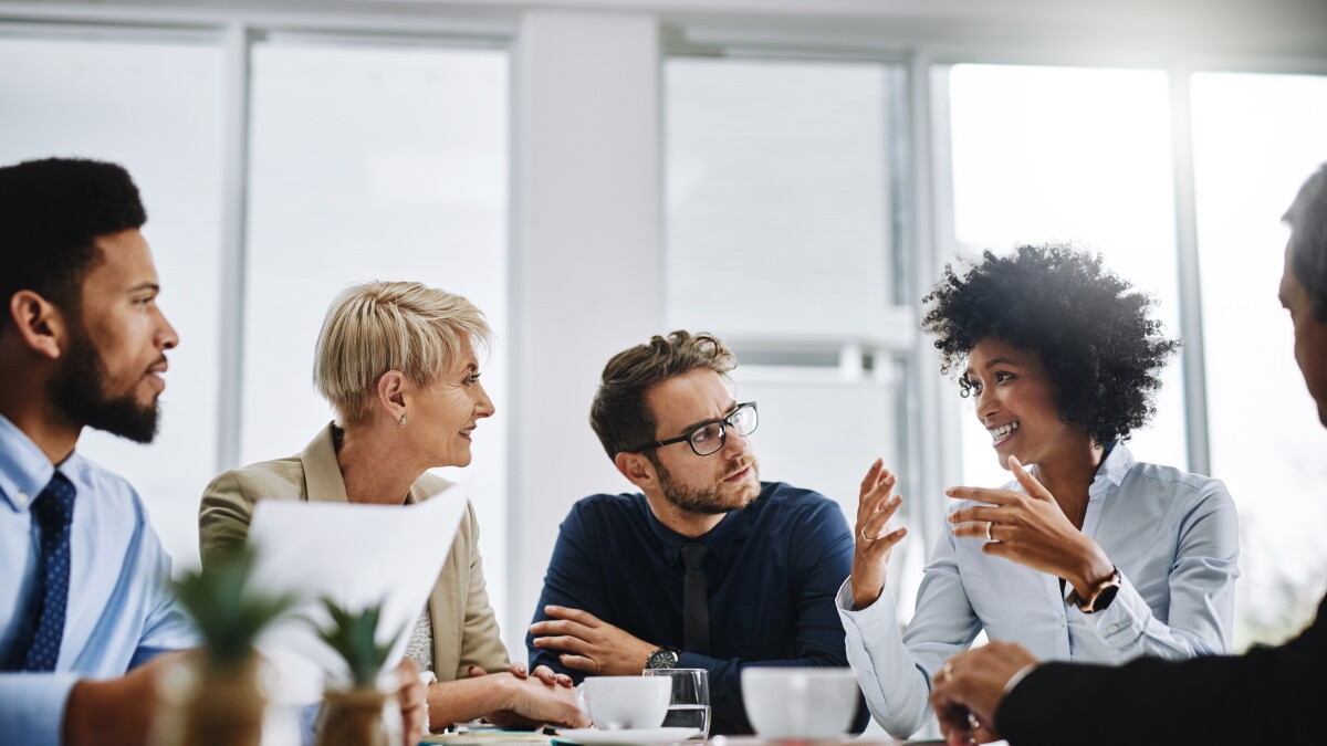 Diverse professionals in a bright meeting room engage in a lively group discussion around a table with coffee cups.